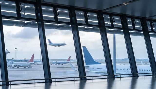 Airport terminal window framing jets on wet tarmac under overcast sky with colorful tails