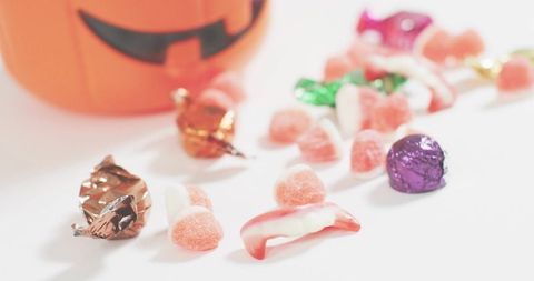 Pastel halloween candy scattered on white surface, jack-o-lantern bucket blurred closeup