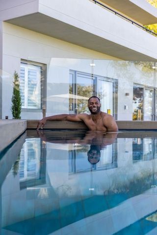 Smiling african american man relaxing in rooftop pool with modern glass railing