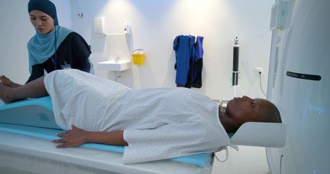 Radiology technologist positioning patient on ct scanner table wearing hijab and gown