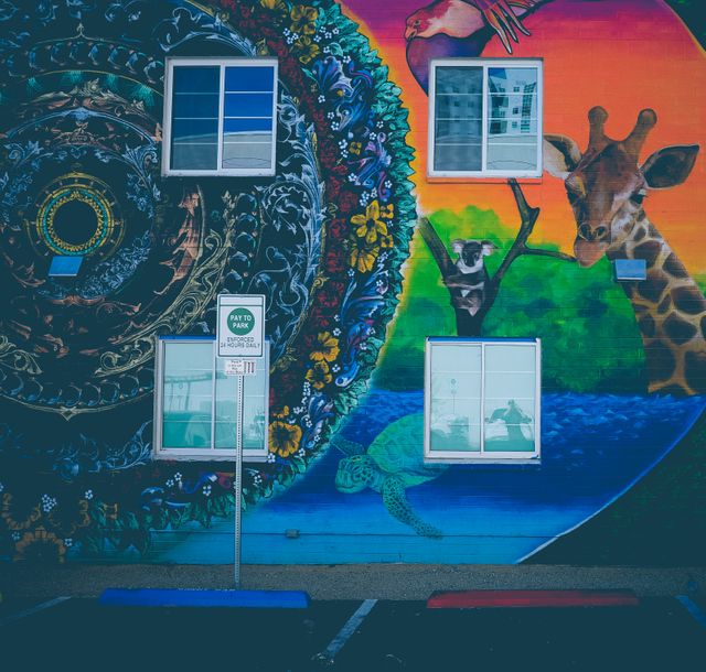 This mural features a vibrant and intricate design with wildlife elements including a giraffe, a turtle, a lemur, and a hummingbird set against abstract cosmic shapes on a building wall. Perfect for urban and cultural projects, art and decor websites, or educational materials about public art.