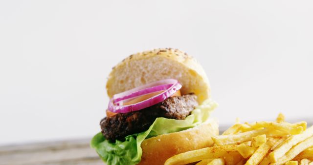 Juicy cheeseburger topped with fresh lettuce, tomato, and red onion, served with a side of crispy French fries. Great for promoting fast food restaurants, menus, or food delivery services. Perfect for illustrating casual dining, comfort food, and traditional American cuisine settings.