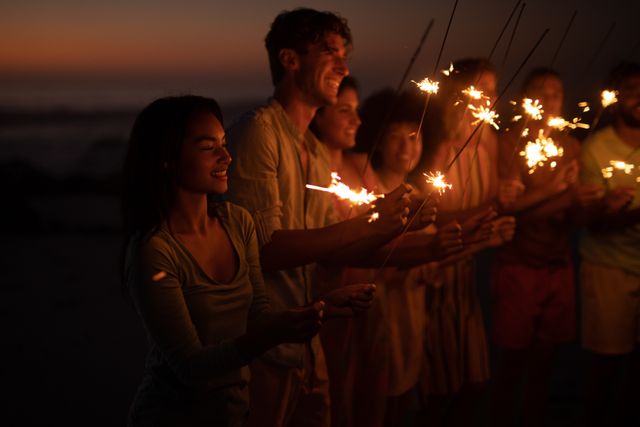 Group of friends from different ethnic backgrounds enjoying a beach evening with sparklers. Perfect for themes of friendship, celebration, summer vacations, and joyful moments. Ideal for use in travel brochures, social media posts, and lifestyle blogs.