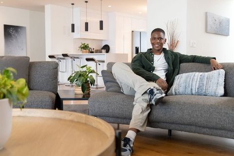 African american man relaxing on modern gray sofa in bright open-plan living room