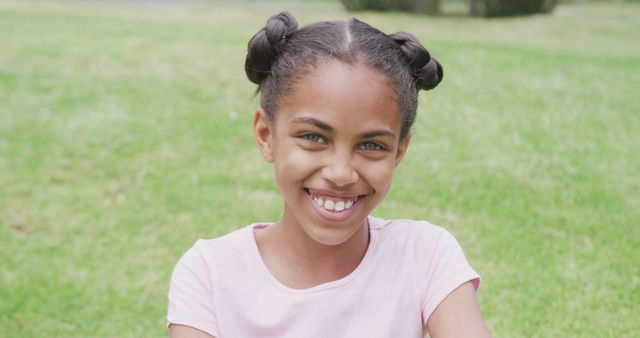 Young African American girl with hairstyle enjoying sunny day in a park, smiling broadly. Ideal for child-related content, family-focused advertising, summer activities promotions, or representing happiness and youthful energy. Perfect for blog posts about parenting, outdoor activities, or photo essays on child development.