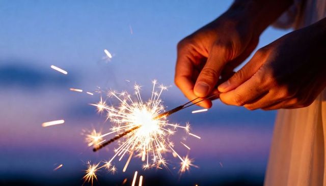 Holding sparklers at twilight producing warm sparks and soft sunset glow