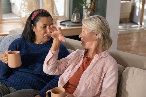 Mature multicultural women sharing coffee and lively conversation on cozy sofa