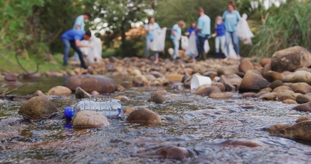 Volunteers wearing blue shirts actively picking up plastic bottles and other trash from rocky riverbed. Rocky stream with clear water showing litter amongst stones. Ideal for showcasing environmental efforts, conservation initiatives, community service projects, and teamwork in nature.