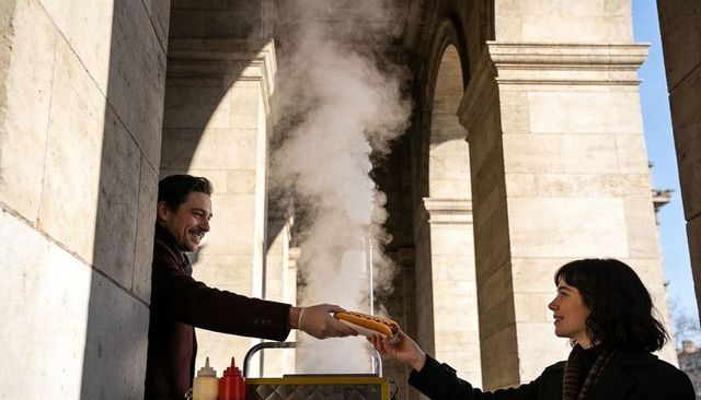 Street vendor handing hot dog to customer at historic stone colonnade, steam rising