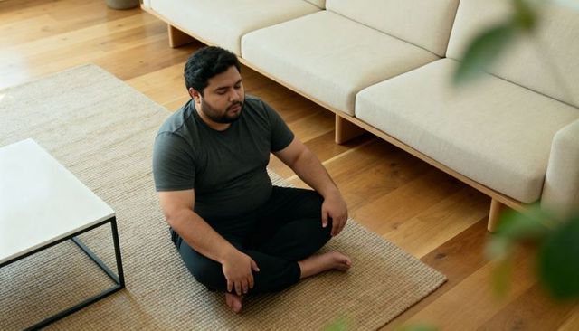 Man meditating cross-legged on rug in minimalist living room with hardwood floor