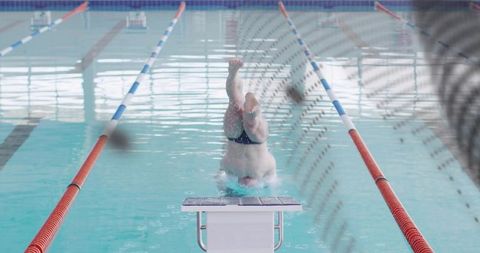 Male competitive diver executing headfirst entry from starting block in indoor lap pool