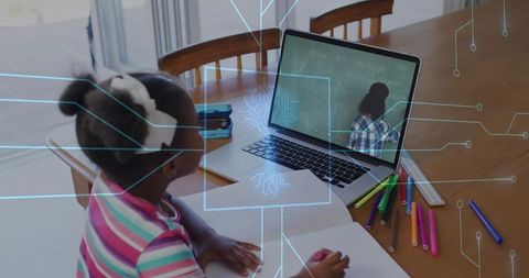 Young girl doing remote learning at home, writing in notebook while watching laptop lesson