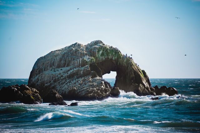Scenic view of a large natural arch on a rocky island surrounded by waves and the open ocean. Ideal for travel blogs, seascape photography collections, nature calendars, and website banners promoting coastal destinations.