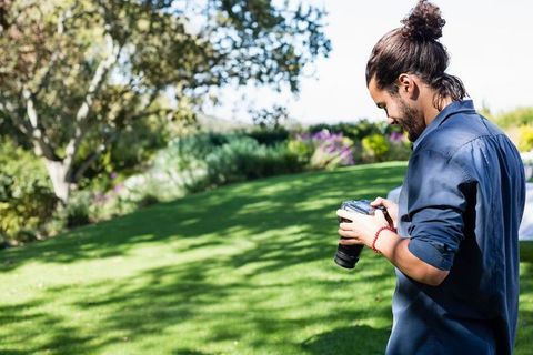Man adjusting dslr camera in sunlit gardens