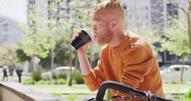 Young man taking a break from biking to drink coffee in an urban park. Ideal for themes of relaxation, healthy lifestyle, and urban living. Good for advertising leisure activities, promoting cafes, or illustrating outdoor enjoyment and urban green spaces.