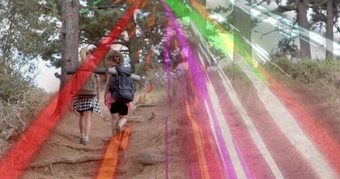 Two women hiking uphill on trail carrying backpacks and pads with colorful light streaks