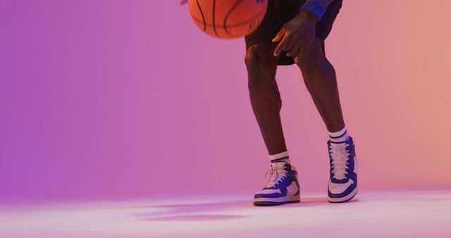 Image of low section of biracial male basketball player with ball on orange to pink background. Sports and competition concept.