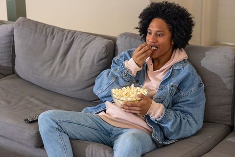 African american man relaxing on couch eating popcorn and watching tv in cozy living room