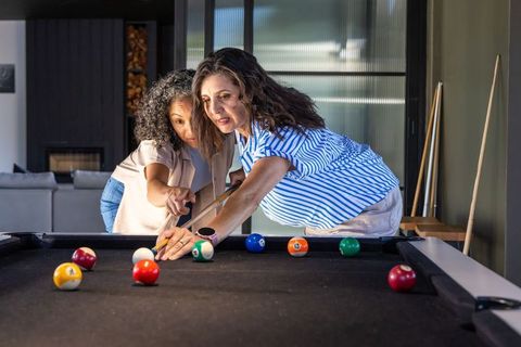 Middle-aged friends leaning over pool table pointing at billiard balls during game night