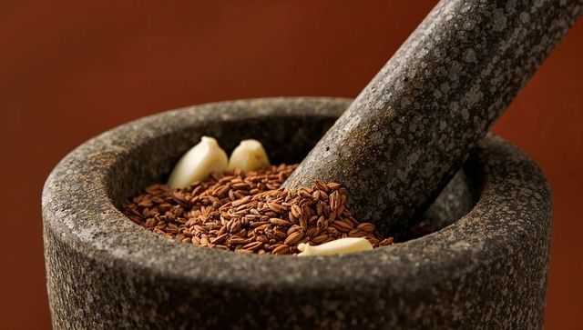 Granite mortar and pestle grinding toasted rice grains with garlic for rustic kitchen