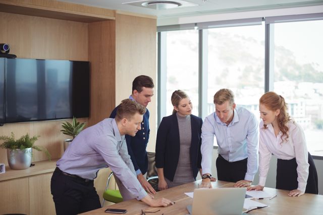 Business professionals gathered around a desk in a modern boardroom, actively discussing project details. Ideal for use in corporate presentations, business websites, blogs about teamwork and collaboration, or marketing materials showcasing professional environments.