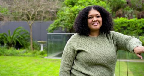 Smiling African American woman leaning on glass railing in backyard wearing green sweater