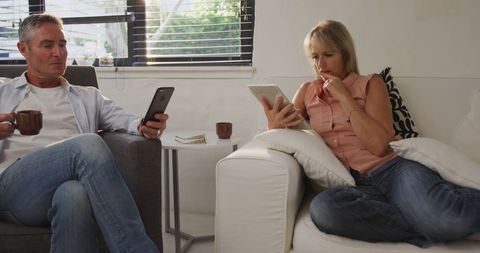 Middle-aged Couple Engaged with Digital Devices in Modern Living Room