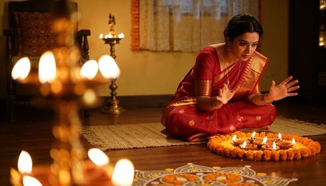 Praying woman in red silk sari lighting diyas and arranging rangoli for diwali ritual