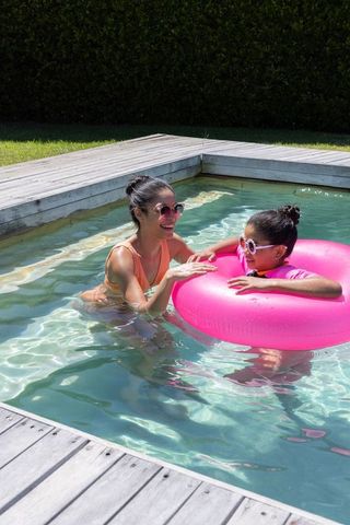African american mother and daughter enjoying backyard pool with pink inflatable ring