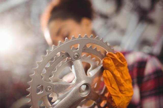 Mechanic examining bicycle gear in workshop, focusing on detailed inspection and maintenance. Ideal for use in content related to bike repair, mechanical engineering, professional training, and maintenance tutorials.
