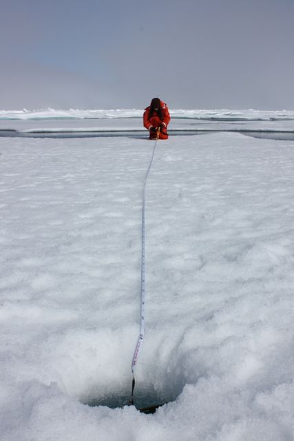 Scientist wearing orange suit measuring ice thickness in Chukchi Sea. July 10, 2011. Suitable for articles on climate research, effects of climate change in Arctic, and scientific expeditions. Ideal for educational content on environmental studies and NASA missions.