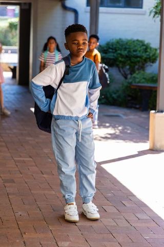 African american boy walking through sunlit school corridor carrying backpack, thoughtful
