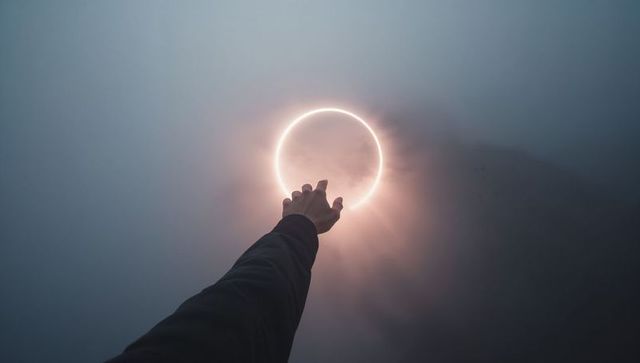Reaching hand towards glowing halo ring in foggy sky, surreal moody futuristic concept
