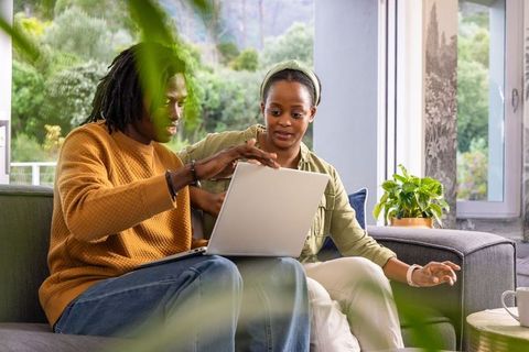African american couple collaborating on laptop in cozy living room with plants for remote work