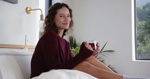 Woman Relaxing on Bed with Tea Beside Window