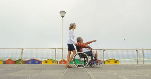 Senior Woman Pushing Man in Wheelchair on Seaside Promenade