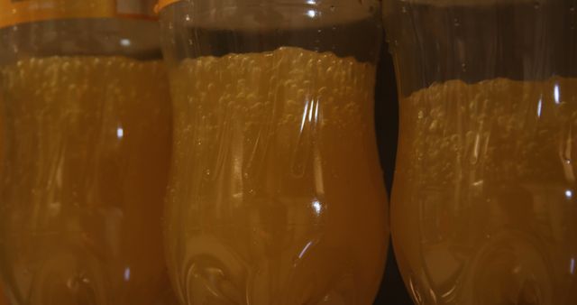Close-up of three bottles filled with sparkling yellow orange beverage, showcasing fizz and refreshing carbonated bubbles inside plastic containers. Ideal for illustrating concepts related to refreshment, summer drinks, beverage ingredients, and commercial beverage advertisements.