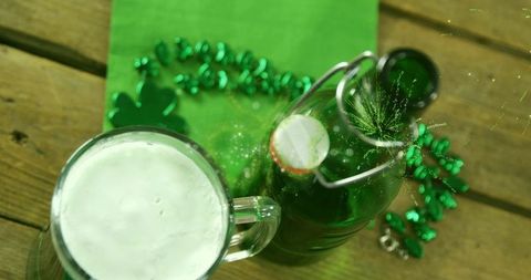St patrick's day foaming beer mug with green flip-top bottle and shamrock beads on wooden table