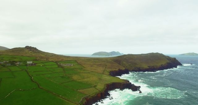 An aerial perspective shows the scenic Irish coastline featuring lush green fields, rugged cliffs, and the expansive ocean. This view highlights Ireland's natural beauty and rural charm. Ideal for showcasing the serene and picturesque landscapes of Ireland, travel blogs, tourism advertisements, and nature-focused websites.