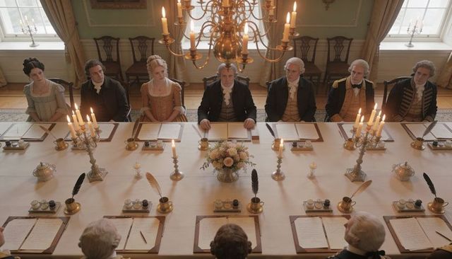 Georgian council chamber with presiding man writing by quill at candlelit long table