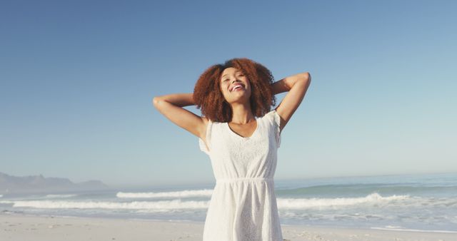 Happy biracial woman smiling on sunny beach by the sea. Summer, free time, relaxation, freedom and vacations.