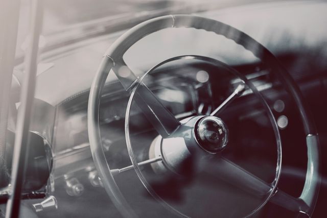 Shows a detailed close-up of a steering wheel in a vintage classic car interior. Ideal for automotive industry promotions, nostalgic advertisements, and retro-themed projects. Can use in blogs about classic cars, historical automobiles, and restoration of old cars.