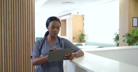 Adult african female nurse checking tablet at clinic reception with stethoscope