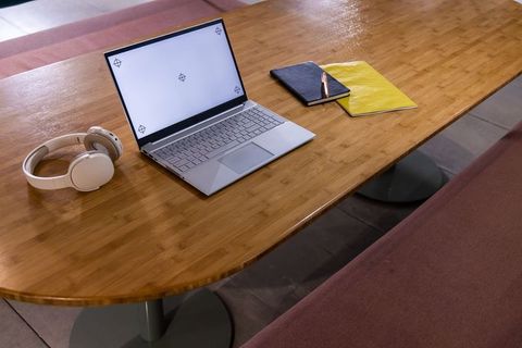 Minimalist coworking desk with slim laptop, wireless headphones, notebooks and copper pen