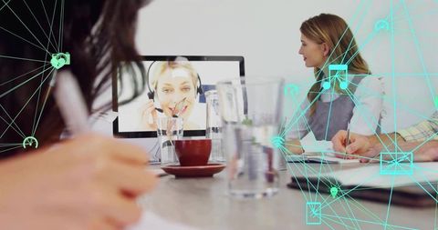Hybrid team collaborating in boardroom taking notes with remote participant on monitor