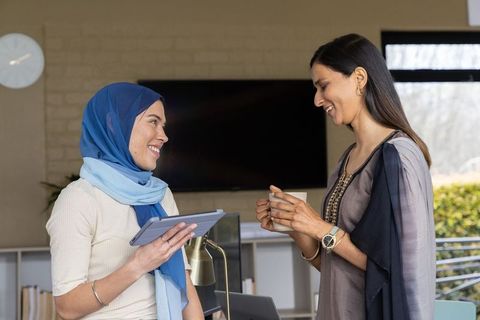 Multicultural female coworkers collaborating in modern office lounge with tablet and coffee