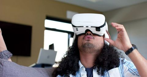 Curly-haired man wearing white vr headset on couch experiencing immersive virtual reality