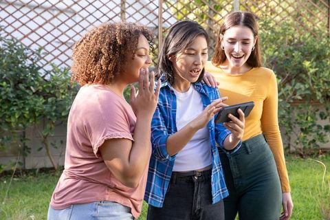 Diverse female friends enjoying digital content in sunny garden