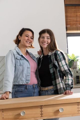 Sunlit friends in casual denim and plaid standing at wooden kitchen island smiling together