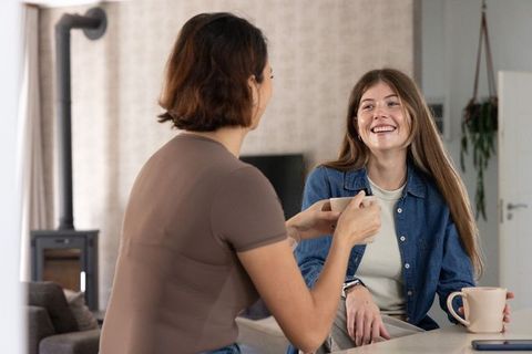 Two friends sharing coffee at kitchen island, smiling conversation in modern home